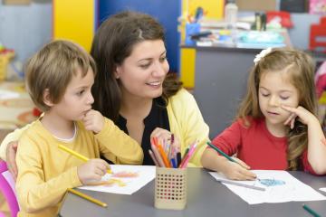 Female preschool teacher at a table with two children